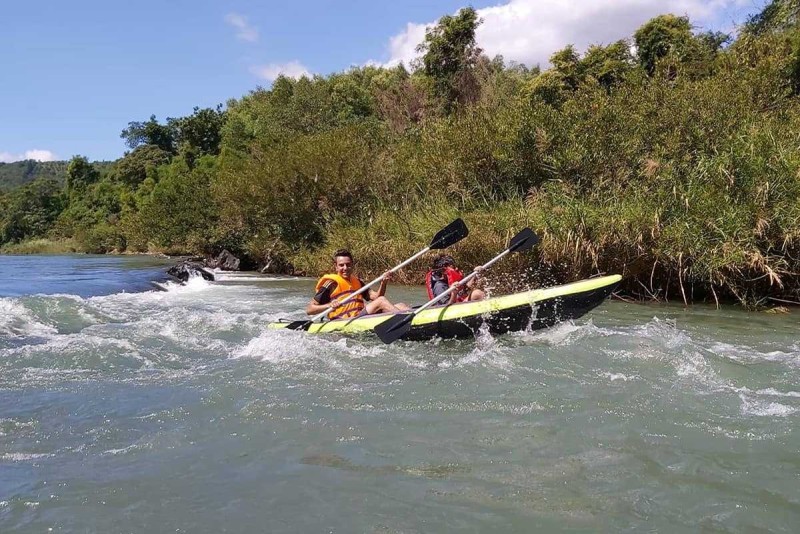Adventurous Kayaking on the Cai River Man and child kayaking through mild whitewater surrounded by riverbank greenery and open sky.