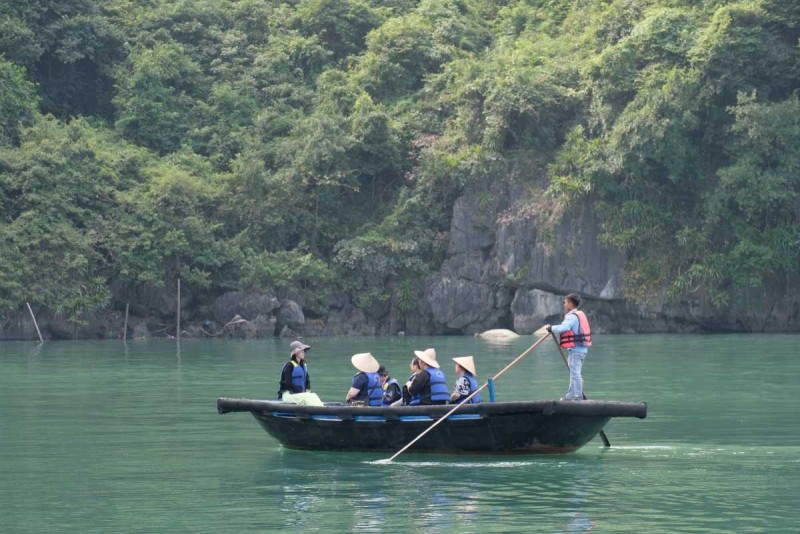 Bamboo boat tour through quiet lagoon in Halong Traditional bamboo boat being rowed across a calm green lagoon in Halong Bay with tourists on board