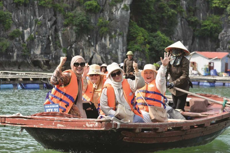 Happy tourists waving on bamboo boat in Halong Bay Smiling women waving from a bamboo boat tour in Halong Bay with cliffs and boats in background