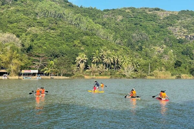 Cai River Kayaking Tours in Nha Trang Multiple kayakers exploring the calm waters of the Cai River surrounded by dense green hills and coconut trees.