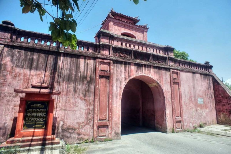 Main gate of Dien Khanh Citadel with red laterite stone walls and arched entry under clear blue sky