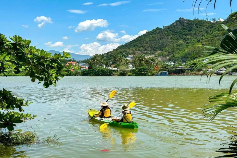 Eco Kayaking on the Cai River Two kayakers in yellow kayak paddling under tree cover with mountain backdrops near Nha Trang.