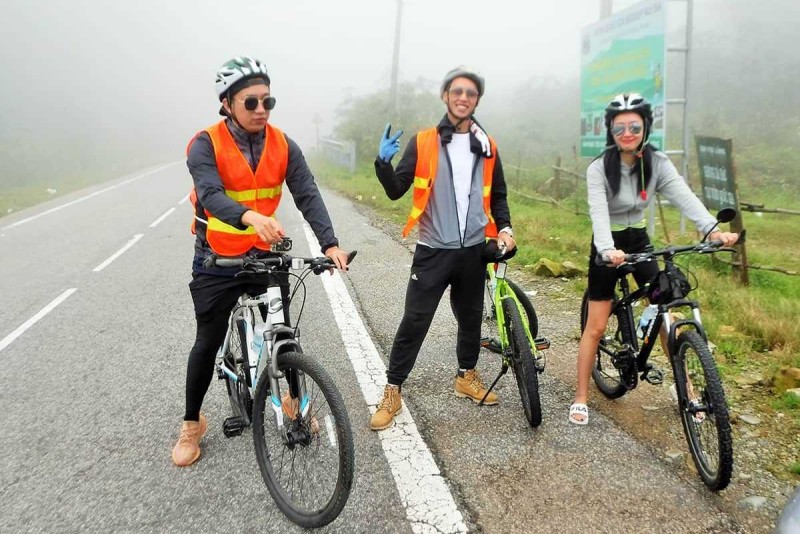 Foggy morning cycling in Nha Trang hills Three cyclists wearing safety vests and helmets pause on a misty roadside during a Nha Trang mountain ride