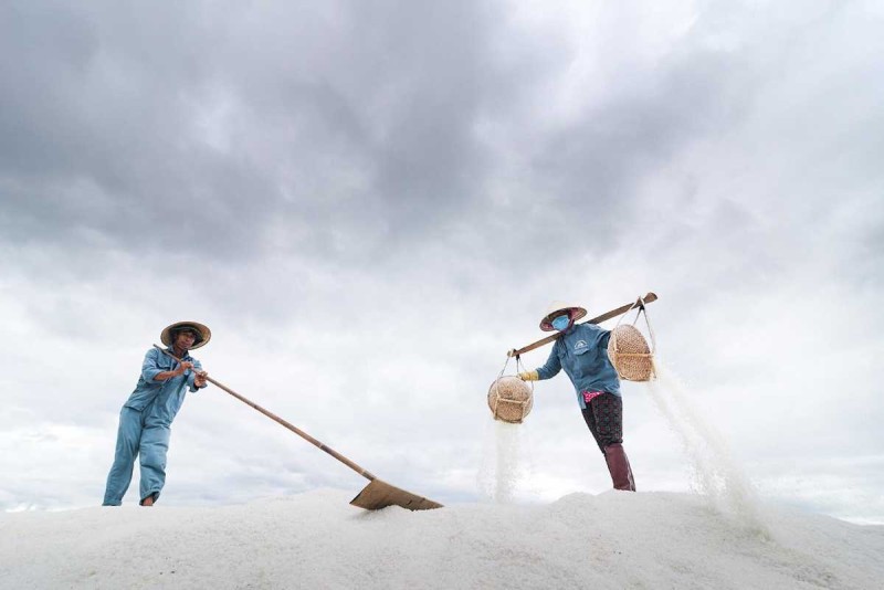 Salt workers pouring white salt from baskets at Hon Khoi Salt Fields near Nha Trang