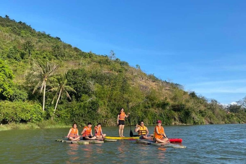 Group of tourists in orange life vests kayaking along the Cai River with lush hills in the background.