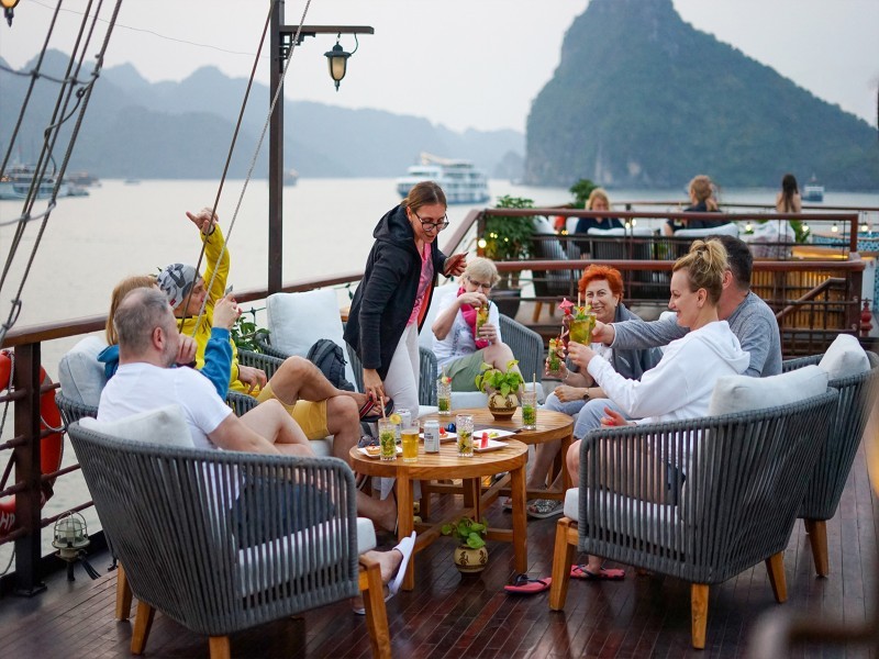 Outdoor dining on a luxury Ha Long Bay cruise Guests enjoy a scenic dinner on a Ha Long Bay cruise with panoramic views and tropical cocktails.