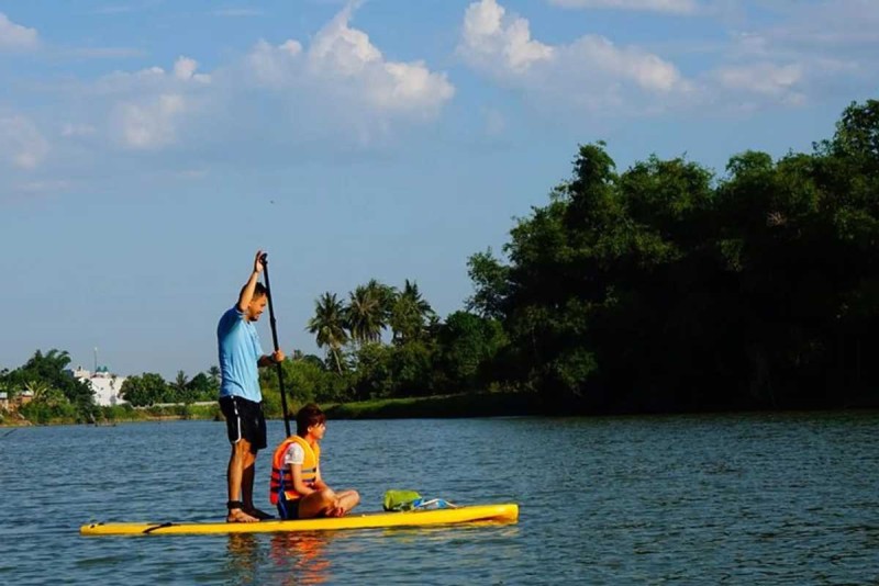 Stand-Up Paddleboarding Cai River Two travelers on a yellow paddleboard gliding through the calm waters of the Cai River under blue skies.