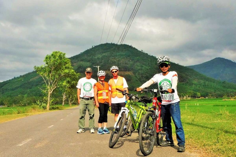 Cyclists pose beside rice paddies in rural Nha Trang Group of cyclists stand near green rice fields with mountain hills behind them outside Nha Trang
