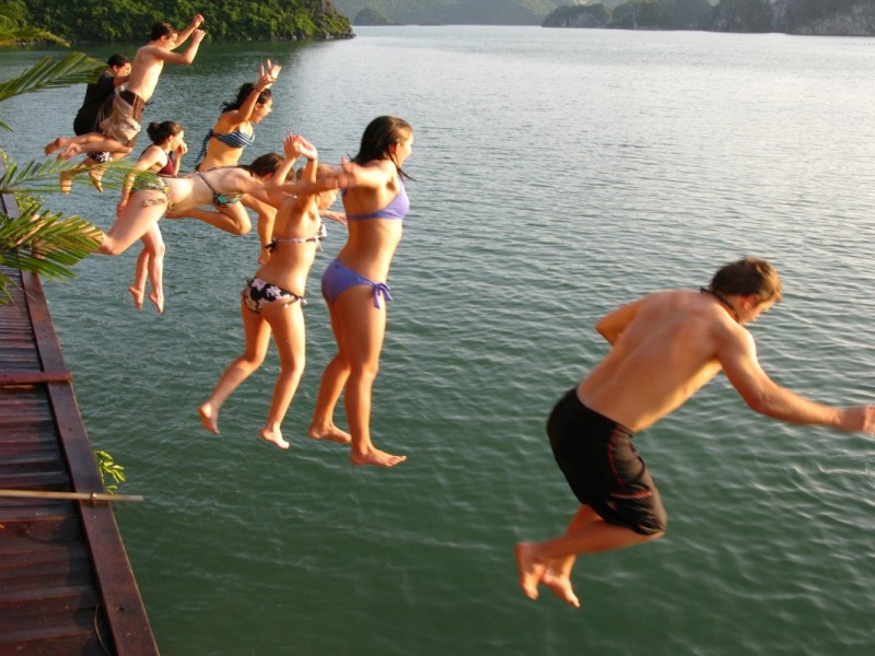 Tourists enjoying a refreshing swim in Halong Bay's emerald waters with limestone cliffs.