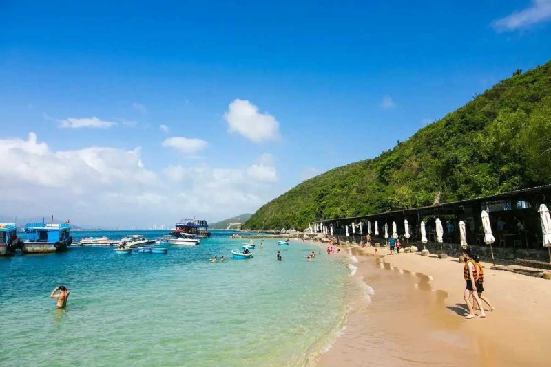 Swimmers enjoying the clear turquoise waters of Tranh Beach near the sandy shore with boats docked in the background.