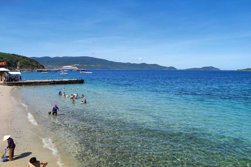 Tranquil Swimming Cove at Tranh Beach Visitors swimming and enjoying the tranquil, clear waters along the shore of Tranh Beach surrounded by green hills.