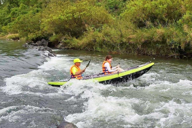 Whitewater Rapids on Cai River Kayakers navigating a small rapid in a bright green kayak, splashing through a rocky channel.