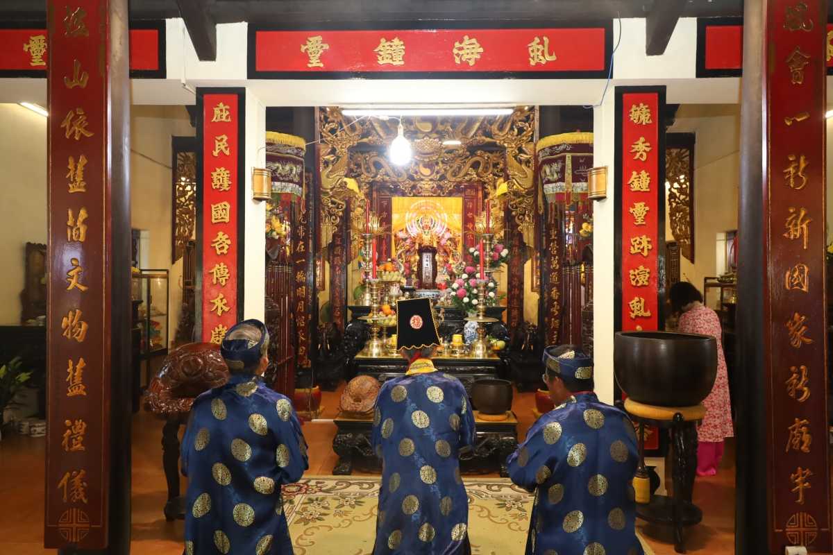 Interior altar and prayer ceremony Inside Am Chua Temple showing a golden altar with devotees in blue prayer robes kneeling in front.