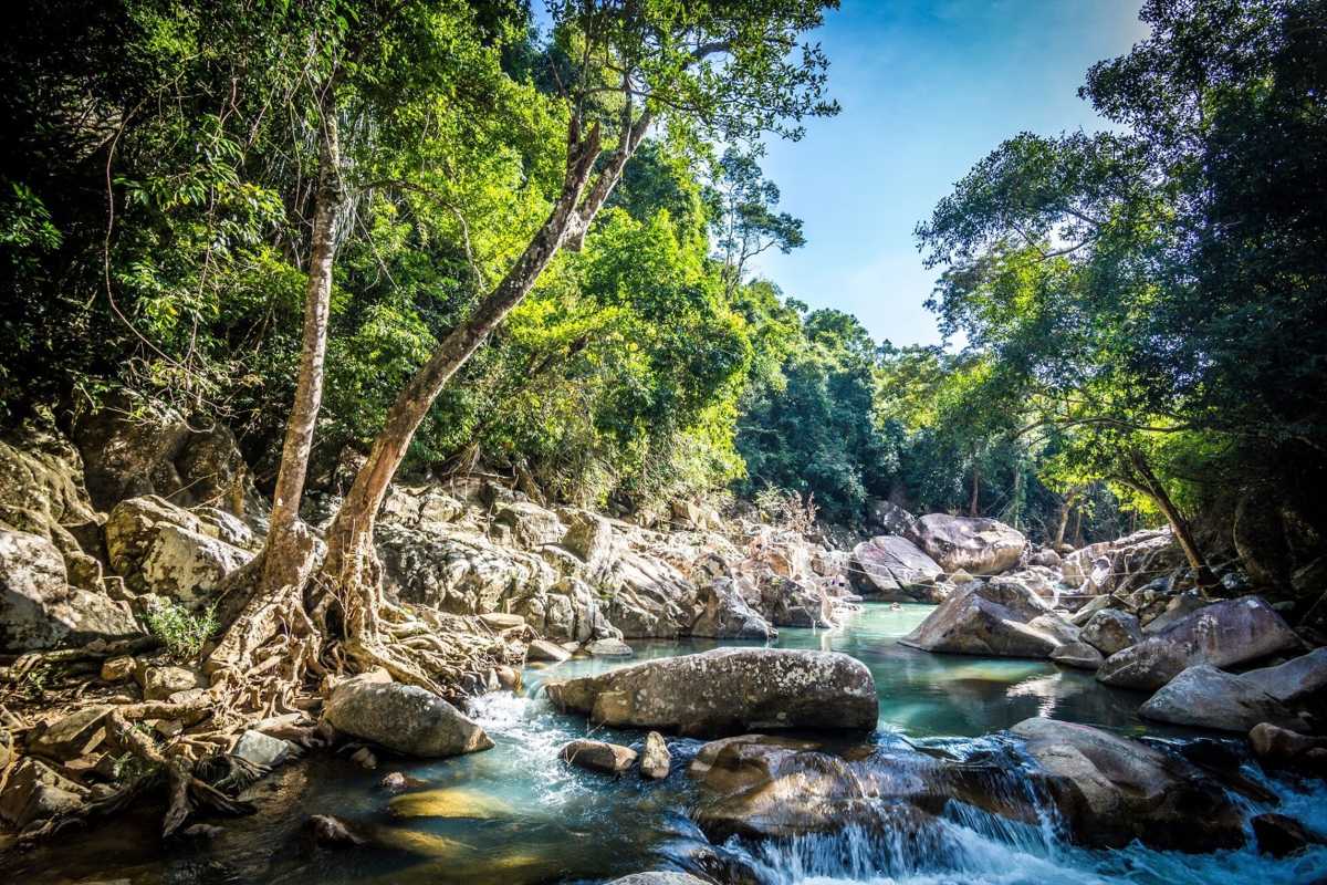 Tropical stream trail near Ba Ho Forest-lined stream at Ba Ho Waterfalls in Nha Trang with large rocks and light shining through.
