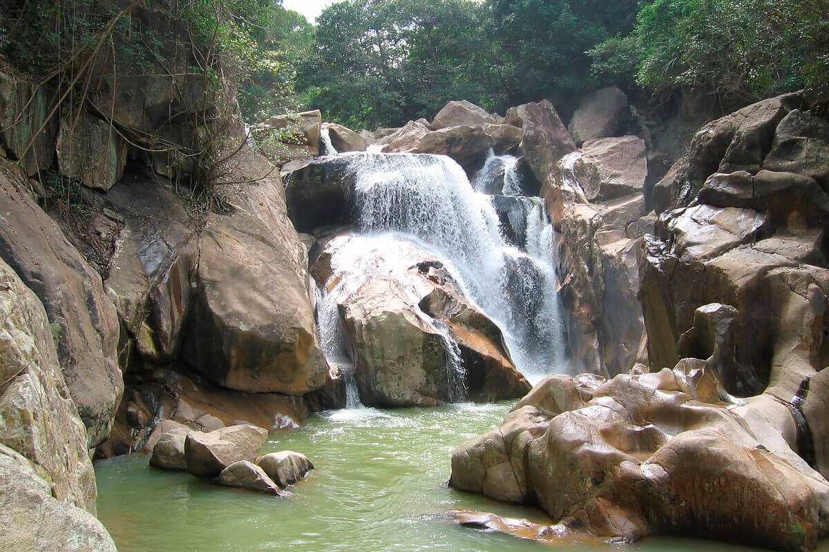 Main cascade of Ba Ho Waterfalls Main waterfall at Ba Ho Waterfalls crashing into a green plunge pool surrounded by large rock formations.