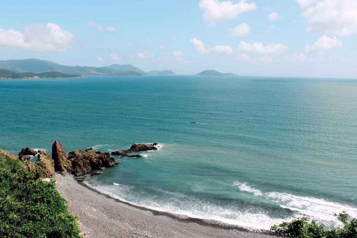 Scenic rocky coastline and waves crashing on Bai Dai Beach Nha Trang's natural shoreline with lush green hills.