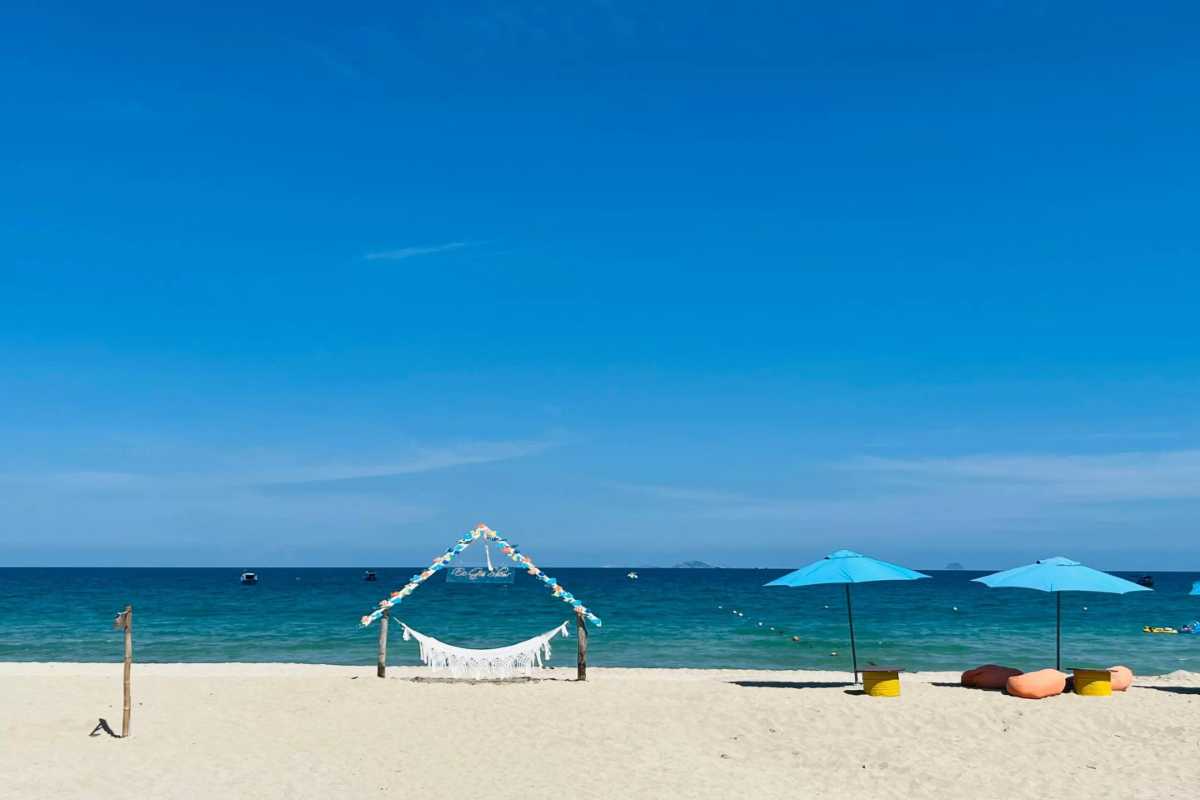 A quiet, secluded beach cove with clear blue waters and lush green hills surrounding Bai Dai Beach Nha Trang.