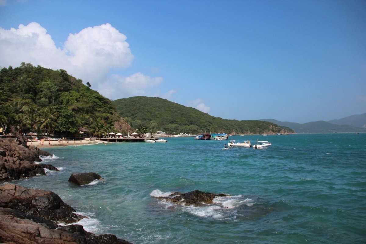 Colorful pebbles on the shore of Bai San Beach with rocky coastline and blue sea