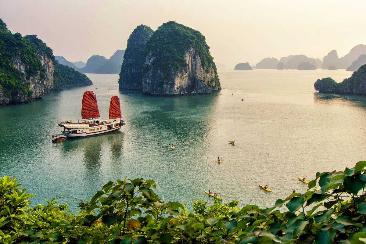 Bai Tu Long Bay Vietnam features a traditional junk boat with red sails cruising among limestone islands.