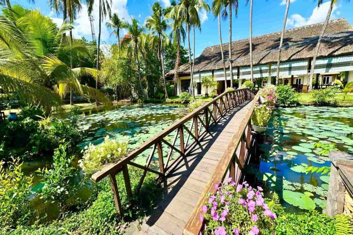 Binh Quoi Tourist Village Ho Chi Minh City features a rustic wooden bridge spanning a scenic lotus pond and lush gardens.