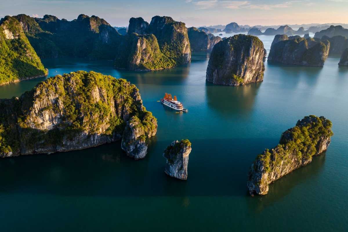 Bo Nau Cave Halong Bay shows towering limestone peaks and a boat cruising through crystal-clear waters.