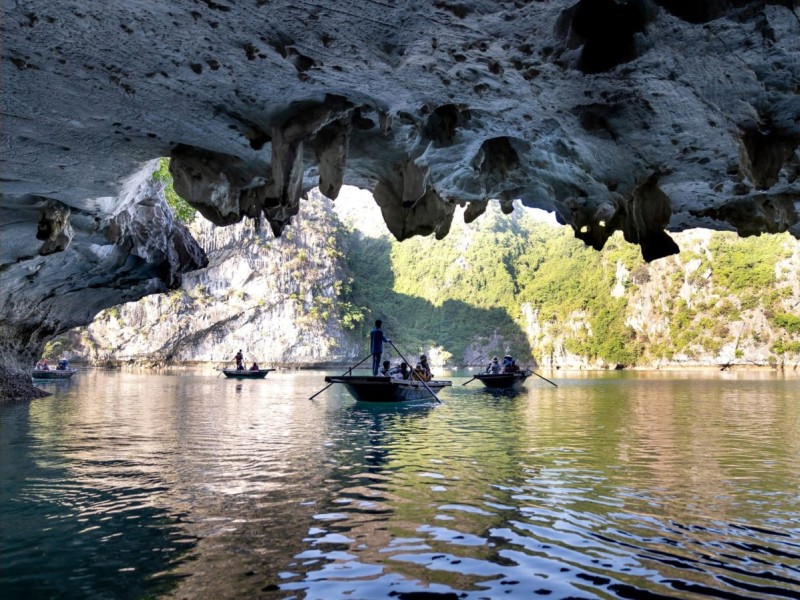 Boat Ride Under Dau Go Cave Entrance in Ha Long Bay Boats navigating through the entrance of Dau Go Cave in Ha Long Bay with scenic views of the limestone cliffs