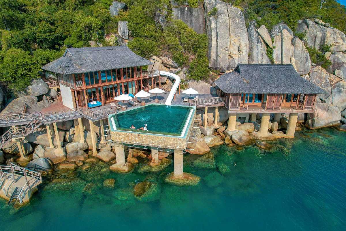 Overwater bamboo houses and infinity pool at Con Sẻ Tre Village surrounded by green hills and clear waters
