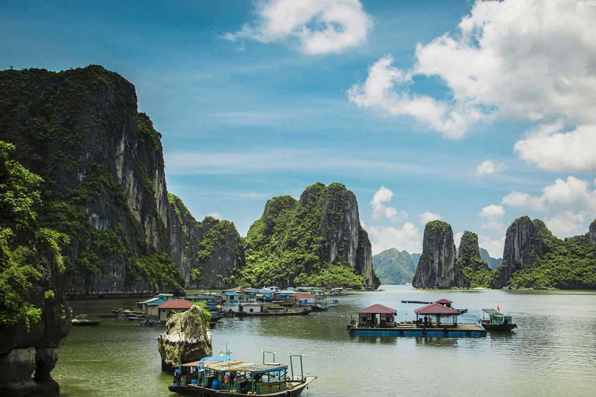 Cruise ship navigating calm emerald waters in Cong Do Island Bai Tu Long Bay, surrounded by limestone karsts.