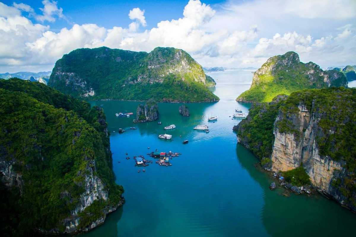 Cruise ship navigating the scenic waters of Cong Do Island Bai Tu Long Bay, surrounded by towering limestone cliffs.