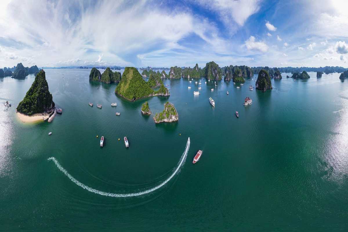 Panoramic aerial view of Bai Tu Long Bay with multiple traditional boats cruising near Cong Do Island’s limestone formations