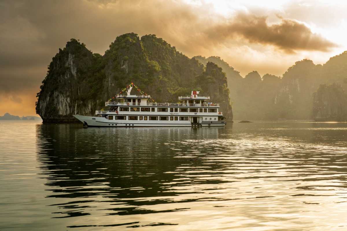 Sunset cruise with limestone peaks silhouetted against a vibrant sky at Cong Do Island Bai Tu Long Bay