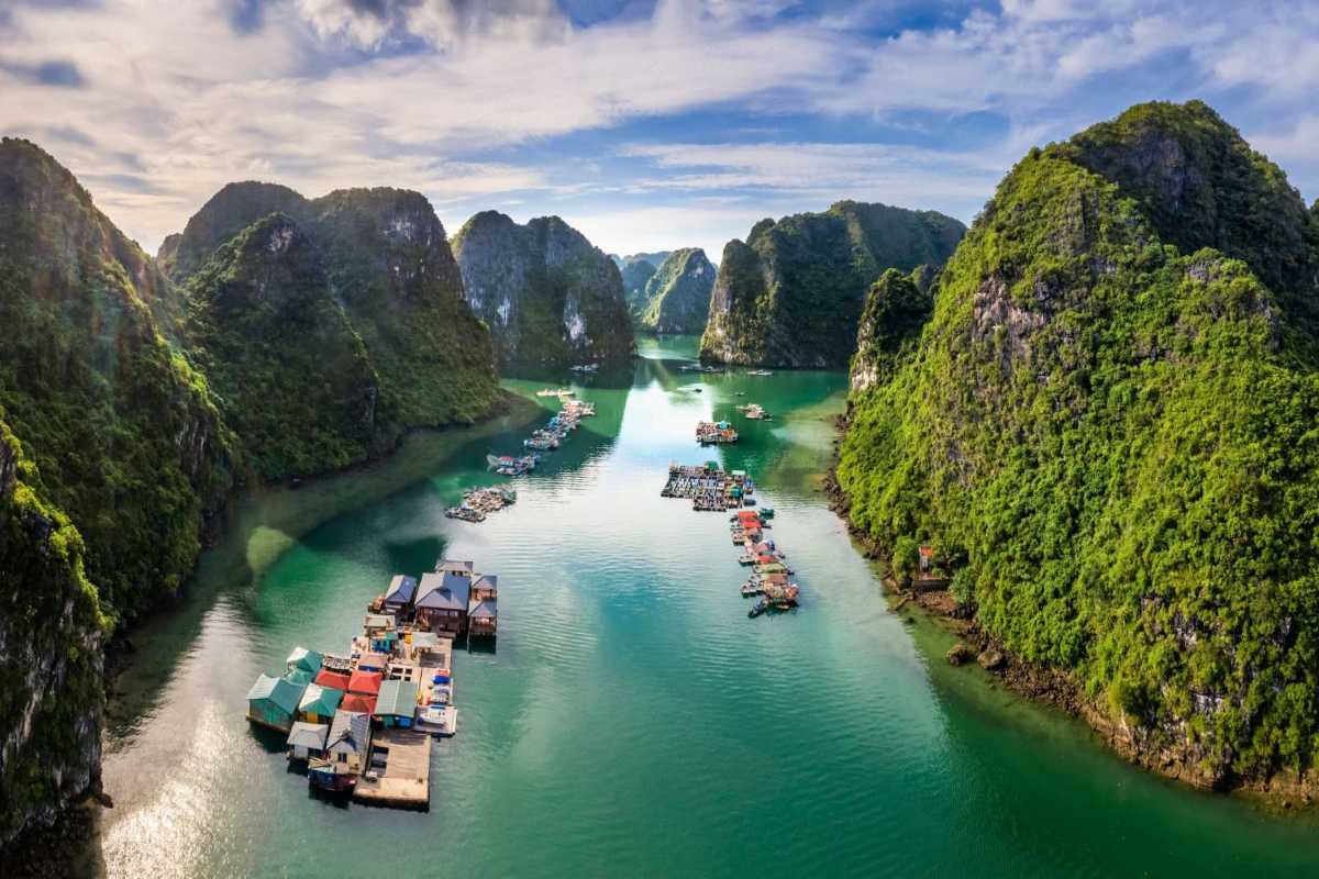 Aerial view of Cua Van Floating Village in Halong Bay showing floating homes and turquoise waters framed by towering limestone cliffs