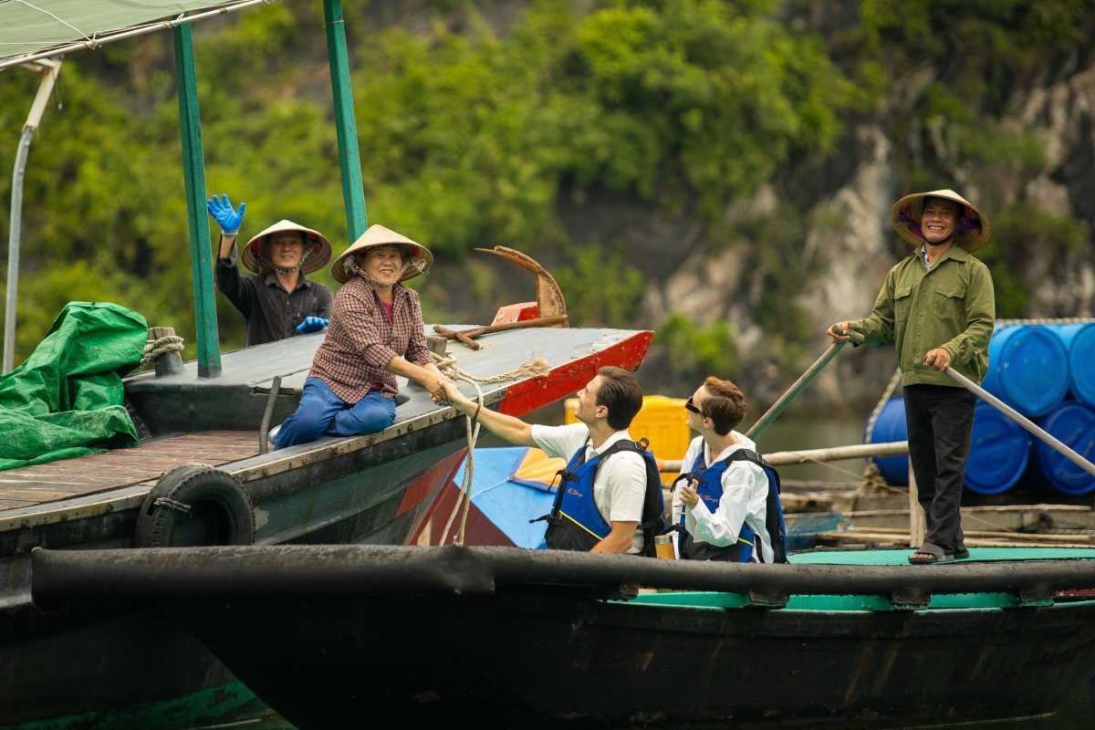 Smiling locals on a boat welcoming visitors to Cua Van Floating Village Halong Bay surrounded by natural beauty
