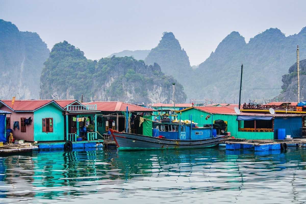 Panoramic view of Cua Van Floating Village with boats, homes, and limestone karsts under a cloudy sky