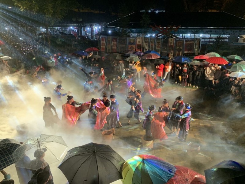 Crowds enjoying traditional cultural festivities at the Sapa Stone Church at night, with colorful umbrellas and lights.