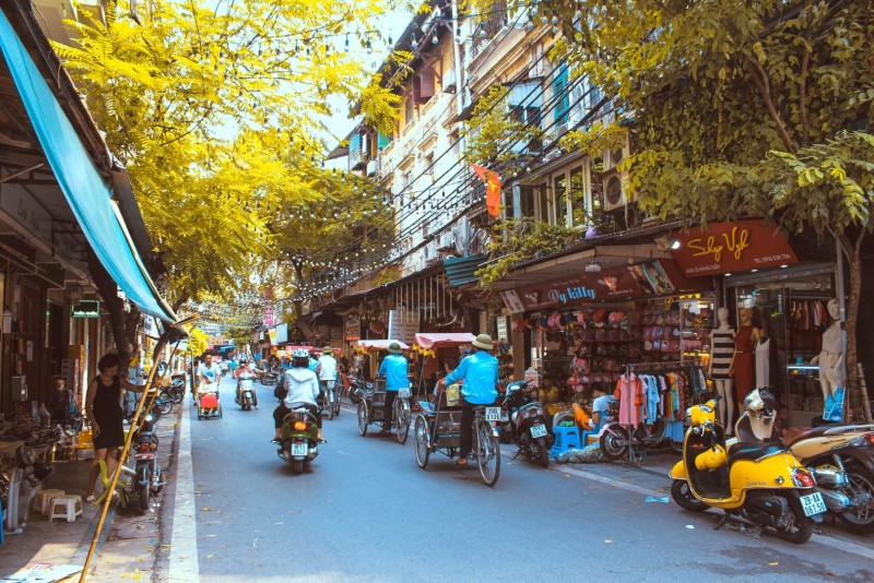 Cyclo Ride through Hanoi Old Quarter Market Street Cyclo riders moving through a bustling street in Hanoi’s Old Quarter with shops on both sides