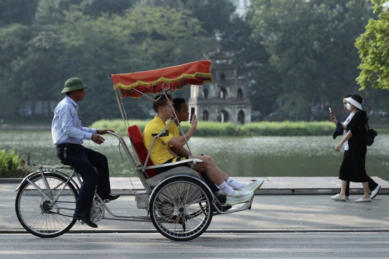 Cyclo Tour by Hoan Kiem Lake with Tourists Cyclo driver pedaling two tourists by Hoan Kiem Lake in Hanoi