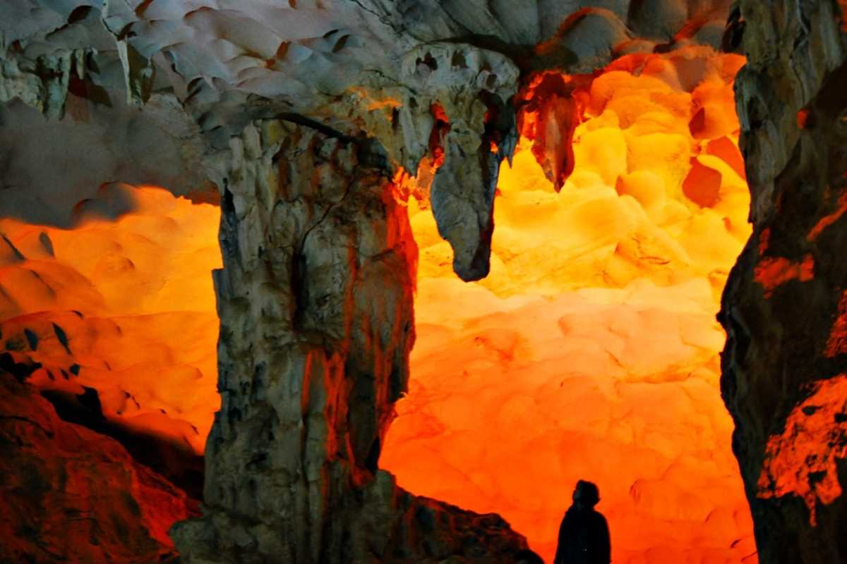 Bright orange rock formations and stalactites under warm lighting inside Dau Go Cave Halong Bay.