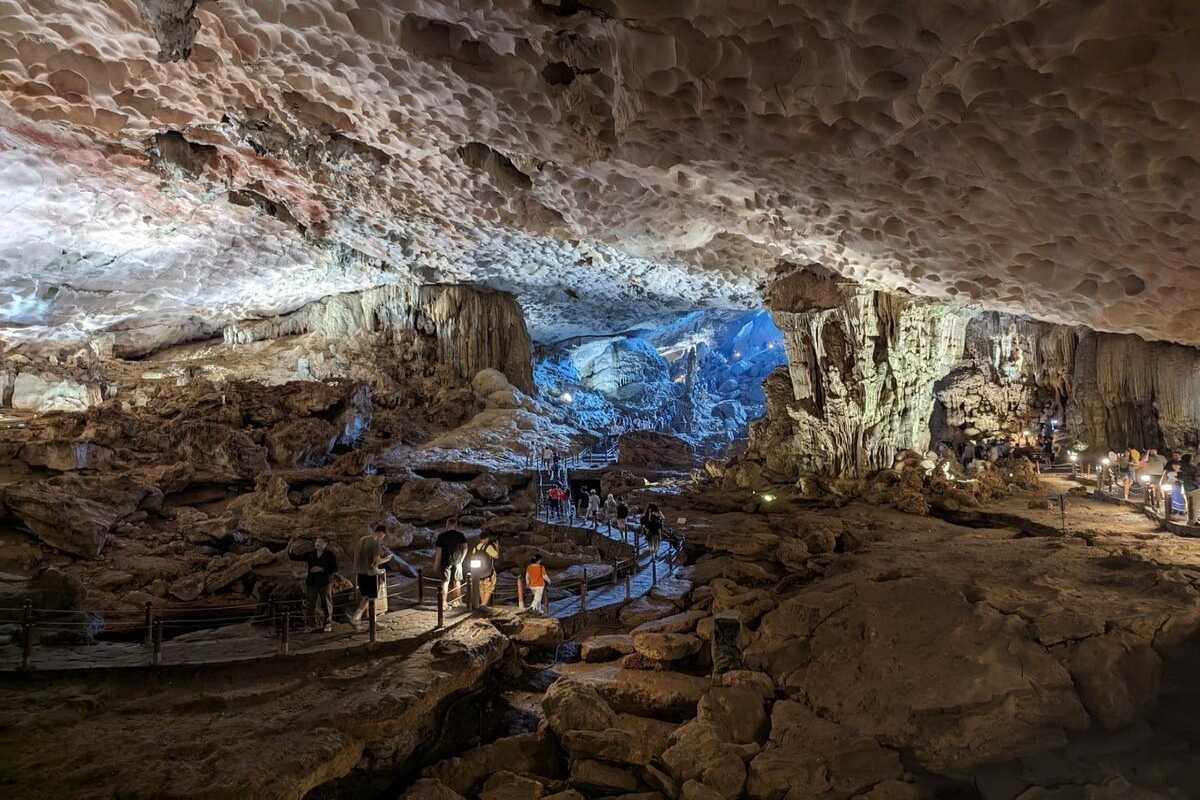 Illuminated stalagmites and cave formations with tourists walking along lit pathways inside Dau Go Cave Halong Bay.