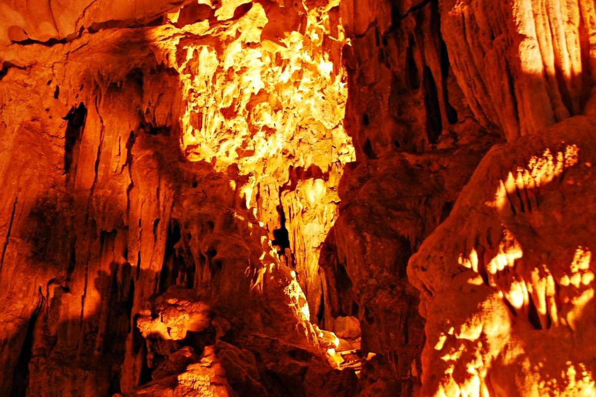 Group of visitors exploring the vast interior of Dau Go Cave Halong Bay with colorful illuminated formations.