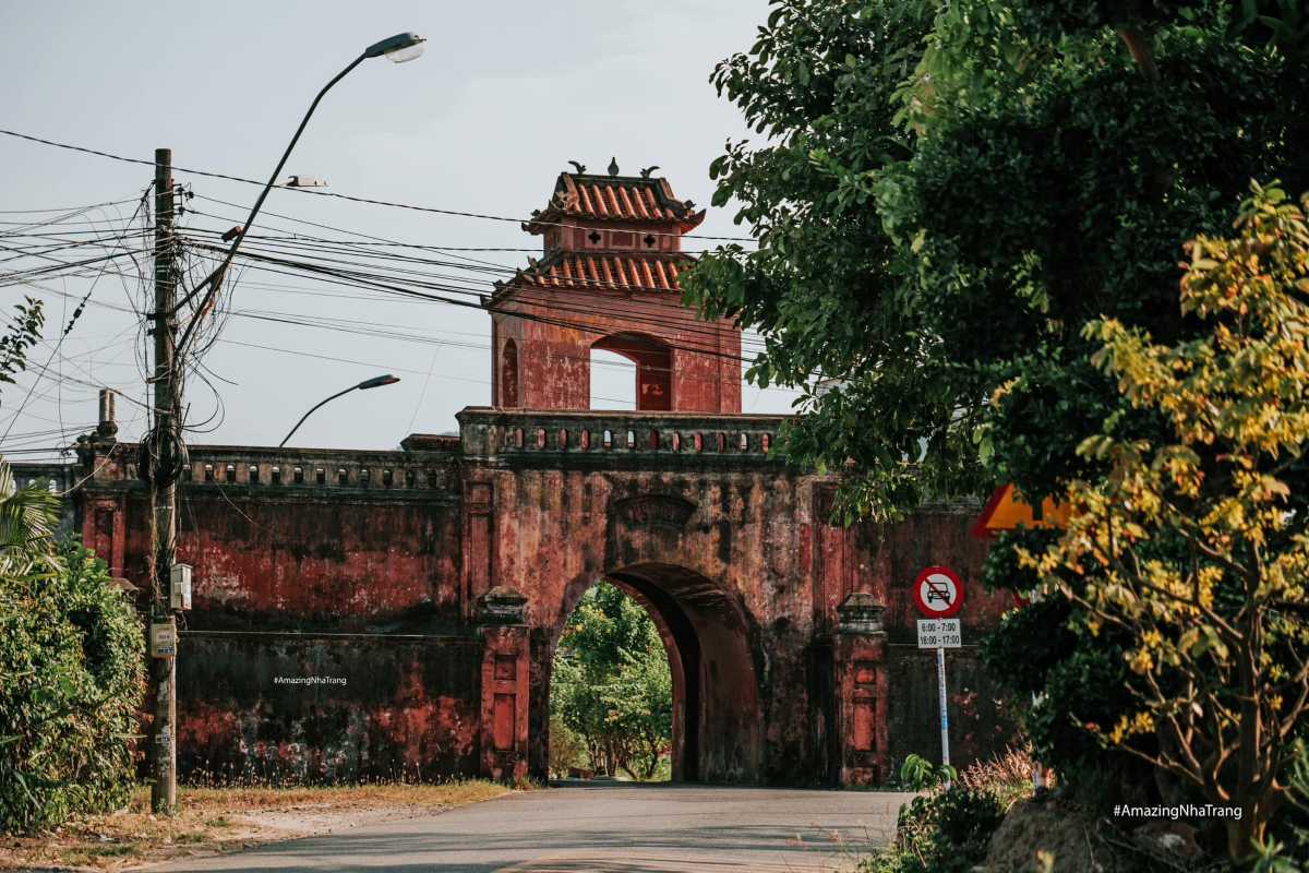 Side view of Dien Khanh Citadel’s red brick gate partly covered by trees and power lines.