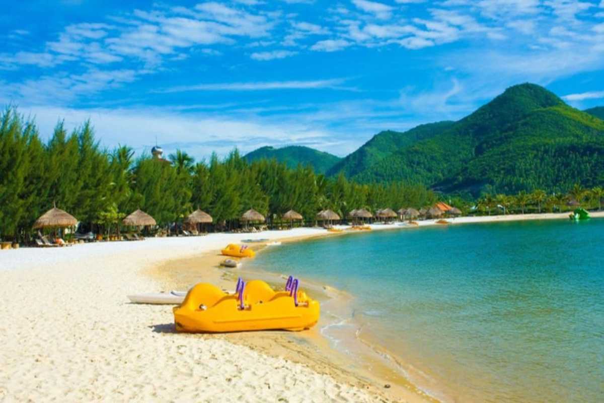 Doc Let Bay and Forested Backdrop View of Doc Let Beach with calm bay waters, green-covered hills, and yellow paddle boats lining the shoreline.