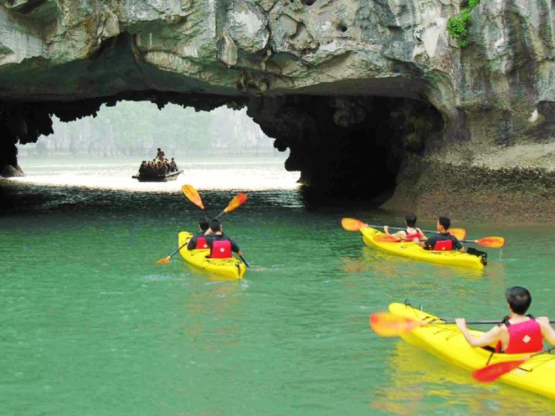 Entering Luon Cave by Kayak, Halong Bay Tourists in kayaks entering Luon Cave in Halong Bay, surrounded by towering limestone formations and calm green waters.