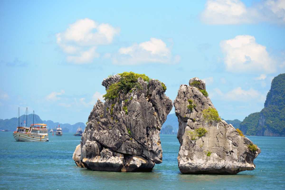 Twilight view of Fighting Cocks Islet Halong Bay with tourist boats anchored near limestone rocks and fading light.