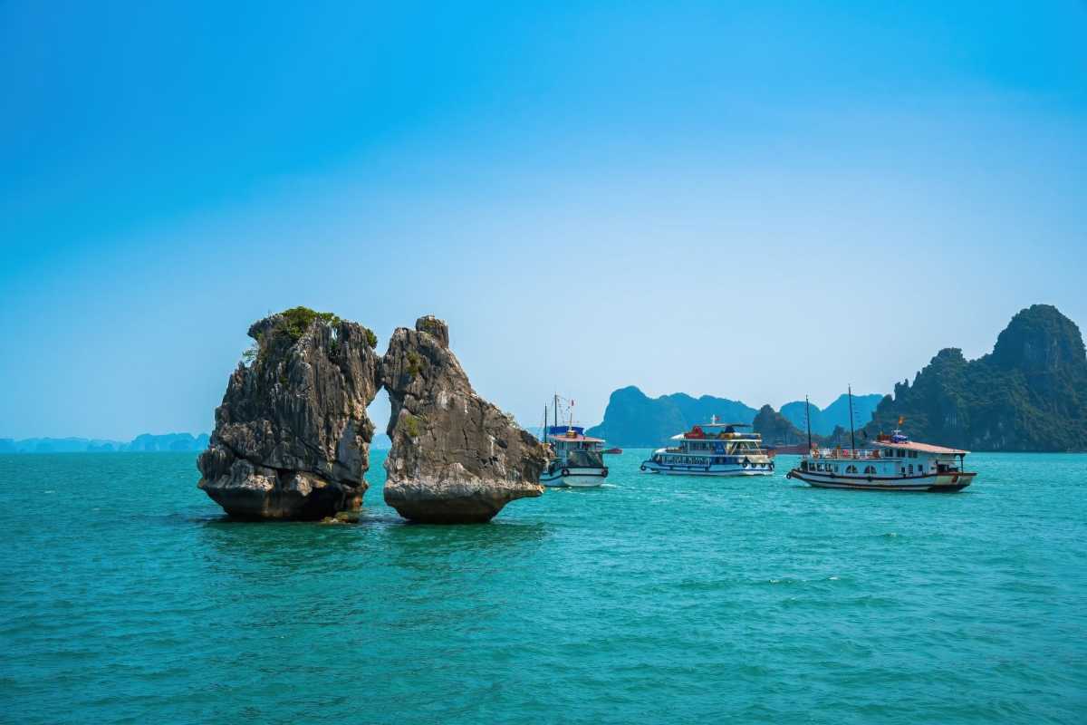 Close-up of Fighting Cocks Islet Halong Bay limestone rocks with nearby tourist boats sailing in calm waters.