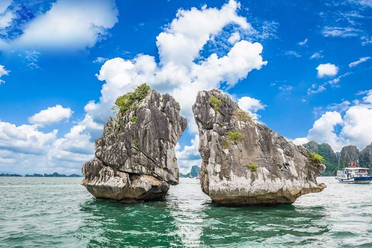 Early morning photo of Fighting Cocks Islet Halong Bay with calm sea waters and misty limestone islands in background.