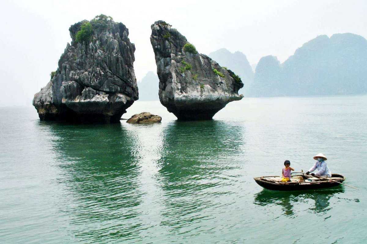 Fighting Cocks Islet Halong Bay glowing in soft morning light over calm sea waters and distant islands.