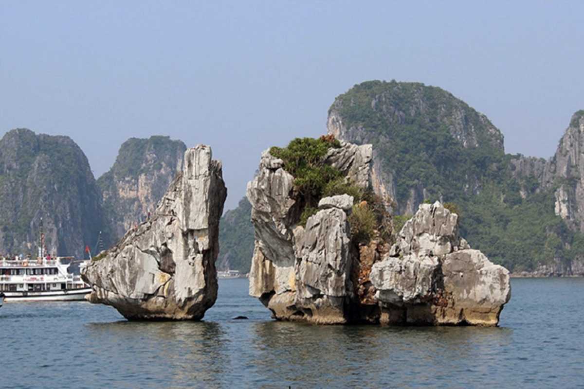 Limestone rock formations of Fighting Cocks Islet Halong Bay surrounded by tourist boats