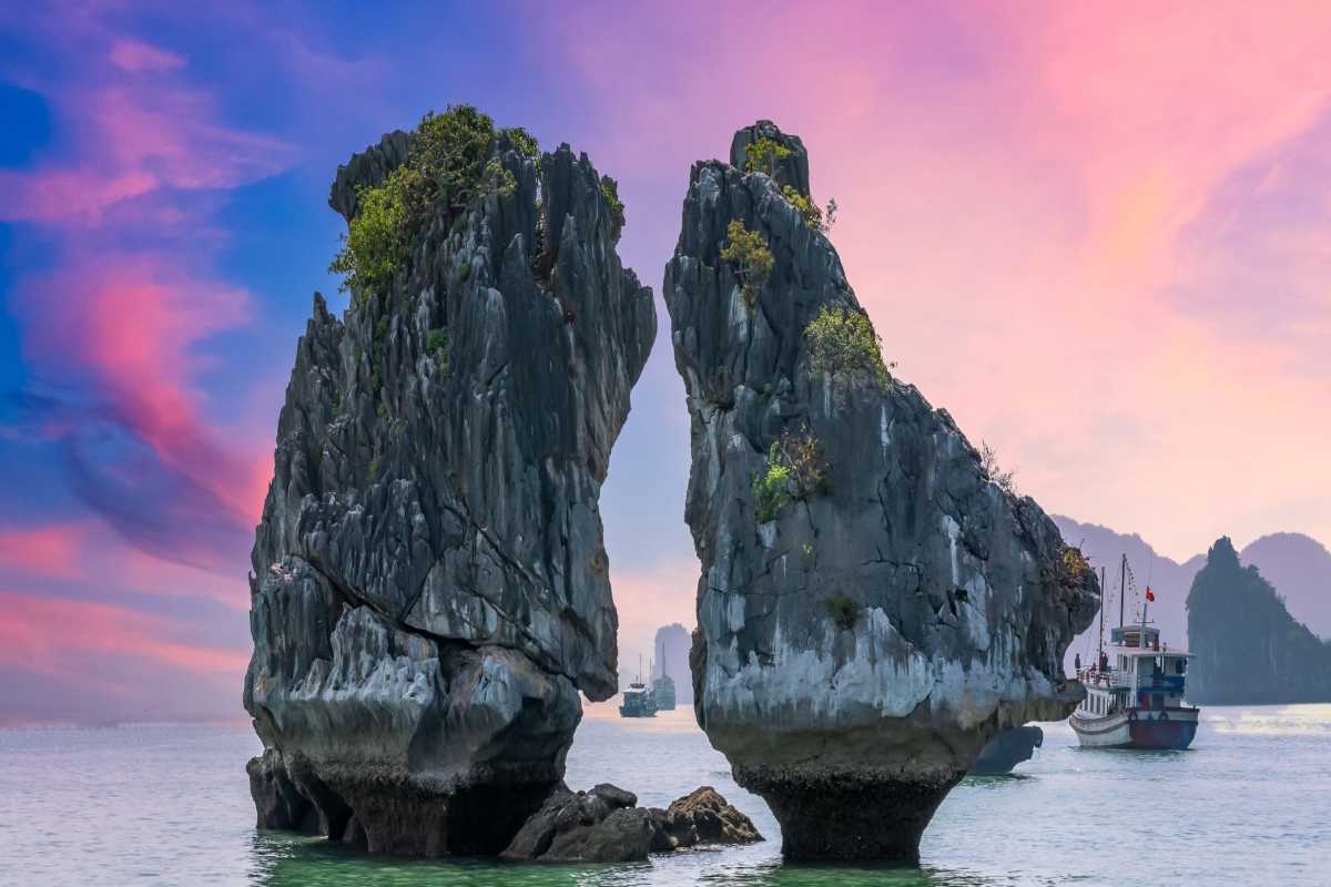 Fighting Cocks Islet Halong Bay bathed in warm sunset light under a colorful sky with surrounding limestone islands.