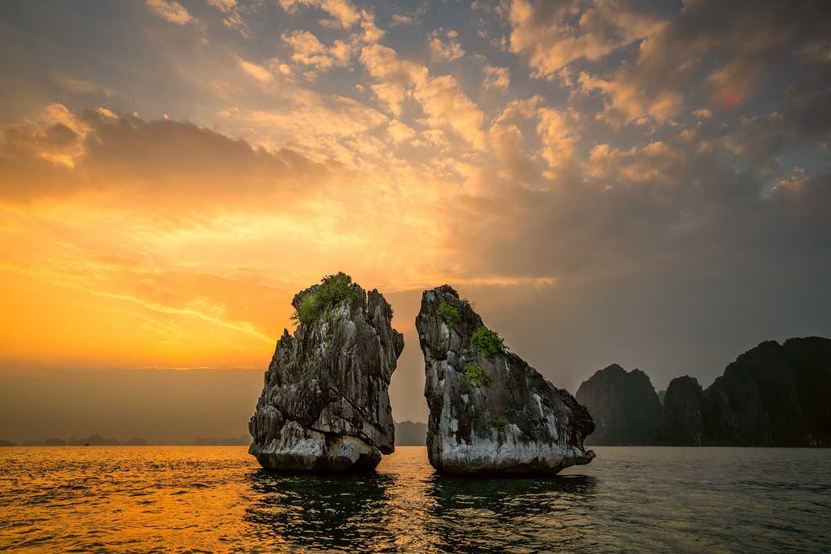 Fighting Cocks Islet Halong Bay at sunset with golden sky reflecting on calm waters